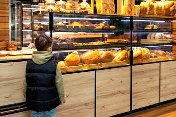 Cute child little boy choosing baked goods or pastry in bakery shop. Little boy buying bread or buns at grocery supermarket and paying by credit card. High quality photo