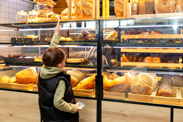 Cute child little boy choosing baked goods or pastry in bakery shop. Little boy buying bread or buns at grocery supermarket and paying by credit card. High quality photo