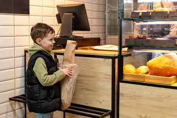 Cute child little boy choosing baked goods or pastry in bakery shop. Little boy buying bread or buns at grocery supermarket and paying by credit card. High quality photo
