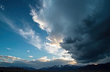 Obraz premium Dramatic cloudscape over mountains with snowy peaks. Sun light is breaking through stormy clouds. Nature scenic view of majestic landscape and weather elements near twilight time.