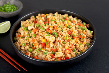 Fried rice with chicken, vegetables and green onions in a black bowl on black background. Asian food. 