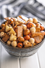 Salted snack. Coated peanuts and mini crackers in bowl on white table.