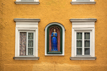Virgin Mary statue on yellow facade with windows
