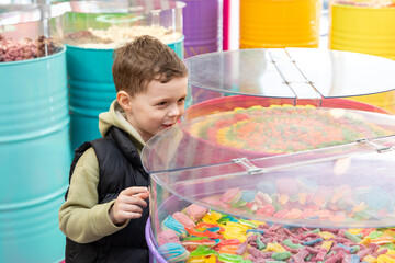 A little boy chooses gummies at a candy store. Unhealthy food for kids. Unhealthy snack. High quality photo