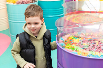 A little boy chooses gummies at a candy store. Unhealthy food for kids. Unhealthy snack. High quality photo