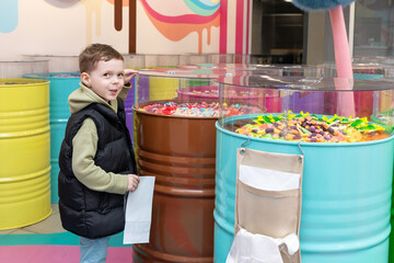 A little boy chooses gummies at a candy store. Unhealthy food for kids. Unhealthy snack. High quality photo