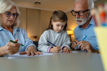 Obraz premium Grandparents, granddaughter drawing together with colored pencils