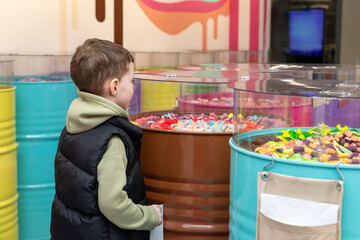 A little boy chooses gummies at a candy store. Unhealthy food for kids. Unhealthy snack. High quality photo