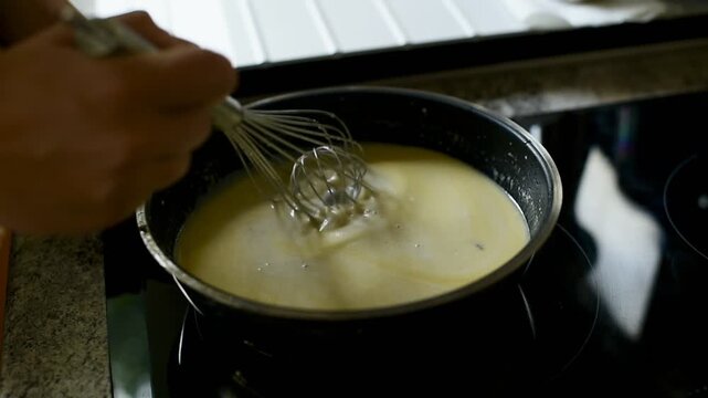 Mens hands stir the bechamel sauce in a frying pan with an iron whisk. FullHD footage. Themes of cooking at home, slow living and everyday routine.