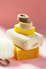 Set of bath accessories, sponges of different sizes and shapes and handmade soap on a pink background.