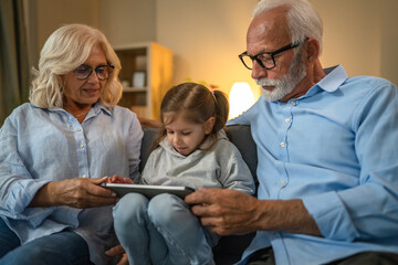 Obraz premium Grandchild using digital tablet with her grandparents at home