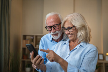 senior husband and wife smile while use mobile phone at home