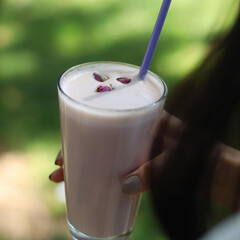 A person is holding a glass of pink liquid with a straw in it