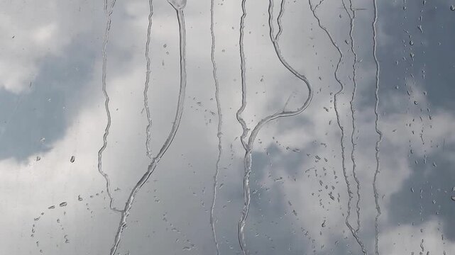raindrops on a window, with a blurred view of a cloudy sky