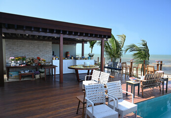 restaurant on the beach, luxury outdoor lounge and party area by the sea, high-end tropical event setting with wooden deck and chairs, exclusive oceanfront resort venue for wedding or celebration