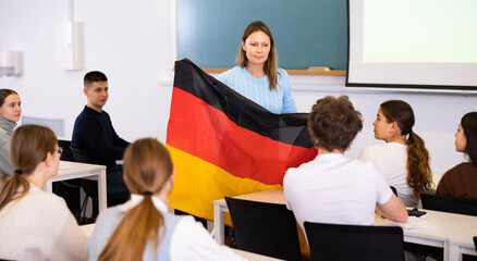 High school teacher holds the flag of Germany in her hands and talks about this country in a...