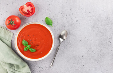 Bowl of tomato puree soup with fresh basil on grey background. Top view. Copy space. Vegan food.