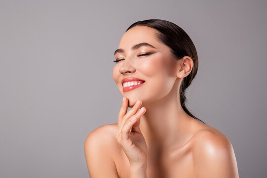 Close up of a young brunette woman with radiant skin and a cheerful smile on a grey backdrop