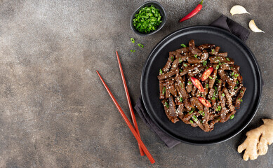 Stir-fried teriyaki beef with sesame seeds and spices on a gray background. Top view. Copy space. Asian cuisine.