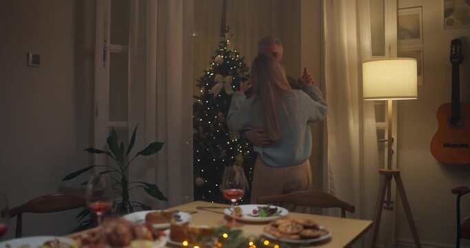 Couple enjoys a cozy dance by the Christmas tree in a softly lit living room during the holiday season