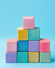 Pastel Wooden Blocks Stacked in Tower on Blue Background, minimal composition of pastel-colored wooden blocks arranged in pyramid shape against clean blue background