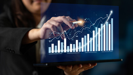 A business professional engages with a transparent digital screen displaying financial graphs and...