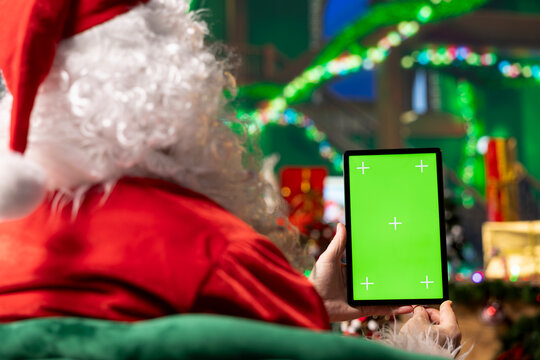 Person wearing red Santa Claus costume using mockup tablet to read letters from kids. Man wearing Xmas hat answering emails received from children using green screen touchscreen device