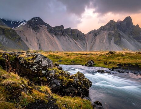 Dramatic mountains beside a flowing river and field under a cloudy sky - Powered by Adobe