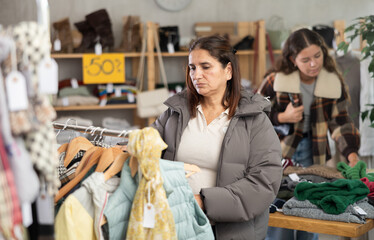 Adult woman buyer choosing clothes for autumn and winter in clothing store