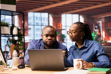 African american man and woman sit at the desk discussing freelance strategies, researching marketing trends to create a helpful report. Couple doing teamwork to finish tasks efficiently.