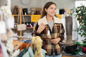 Fashionista girl in shop, go for fitting checkered coat-jacket. Off line clothing store from retailer. Style and fashion type look, modern trends. Outlet, discount store. Customer looks at herself in