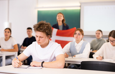 High school teacher tells students about Denmark and holds a Denmark flag in her hands.