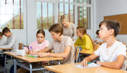 Portrait of diligent schoolboy who writing exercises at lesson in secondary school