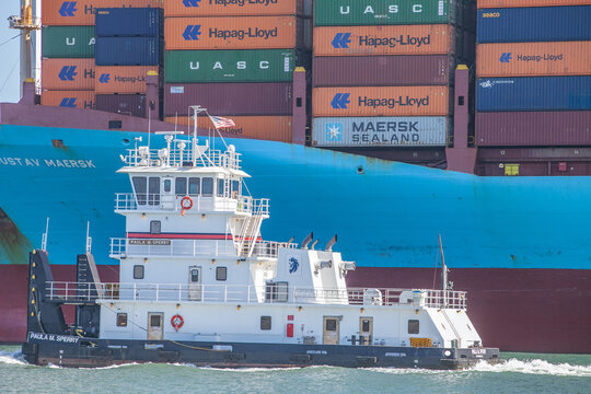 Tugboat guiding container ship loaded with cargo at Port of Oakland under clear sky