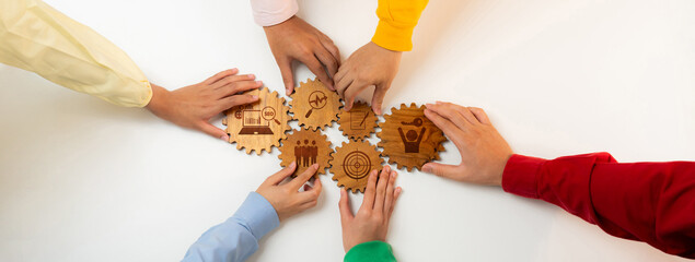 Diverse hands come together to align wooden gears, symbolizing teamwork, strategy, and shared goals...