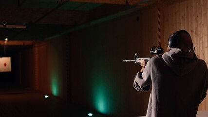 Shooting range customer shooting targets with semiautomatic weapon, having fun. Man at indoor...