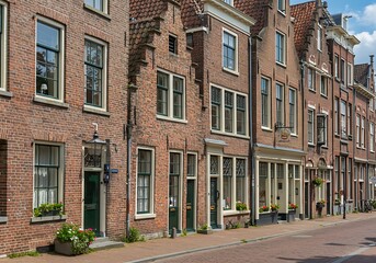 Fototapeta premium DELFT, NETHERLANDS - JULY 29 2021: Facades of authentic colorful brick houses, the left one with stepped gable, in the historical center of Delft, The Netherlands.