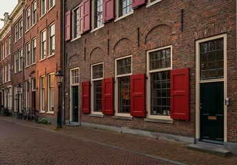 Historic Dutch building with classic red wooden shutters on a windows. The brick facade and large windows with small panes are typical architectural elements of the Netherlands.