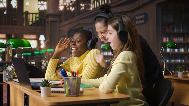 Young students and tutor attending an online class via video call in the library, focused on distance learning and completing a school assignment with other classmates on the network. Camera A.