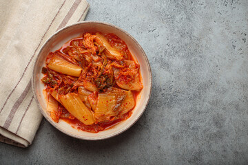 Kimchi, a fermented napa cabbage Korean dish, in a rustic ceramic bowl on a grey concrete...