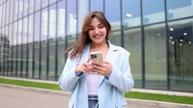 Smiling young woman walking outdoors while texting on her mobile phone. Successful female professional using a smartphone in the city street