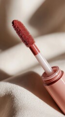 Close-up of a velvet matte liquid lipstick applicator in a deep mauve-pink shade on satin.