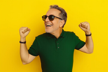 Man in green polo shirt celebrating with raised fists against yellow background. Success concept showing enthusiastic male expressing victory with energetic gesture and vibrant copy space.