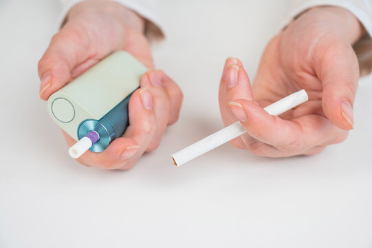 Woman holding regular and electronic cigarette on white background. Tobacco heating systems.
