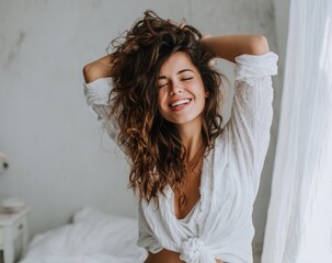 Woman with brown curly hair smiles, arms raised, in a white button down shirt