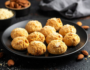 Homemade almond cookies arranged on a black plate with crushed nuts sprinkled on top.
