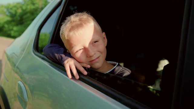 Happy boy child travels by car looking out car window. Summer family travel by private transport. Young boy dreaming smiling. Kid travels with his family. Happy family traveling by car. Boy travelers