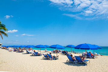 Beach loungers, chairs and beach umbrellas in Fort Lauderdale Beach, with its clear waters and palm trees. Florida, USA, Jan 2019	