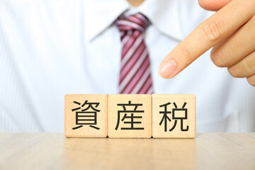 ネクタイ姿の男性が資産税と書かれた文字ブロックを持っている。