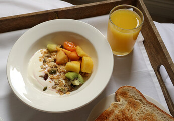 Serving a healthy breakfast with yogurt, granola, fresh fruit, orange juice, and toast in bed. Cotswolds countryside, England